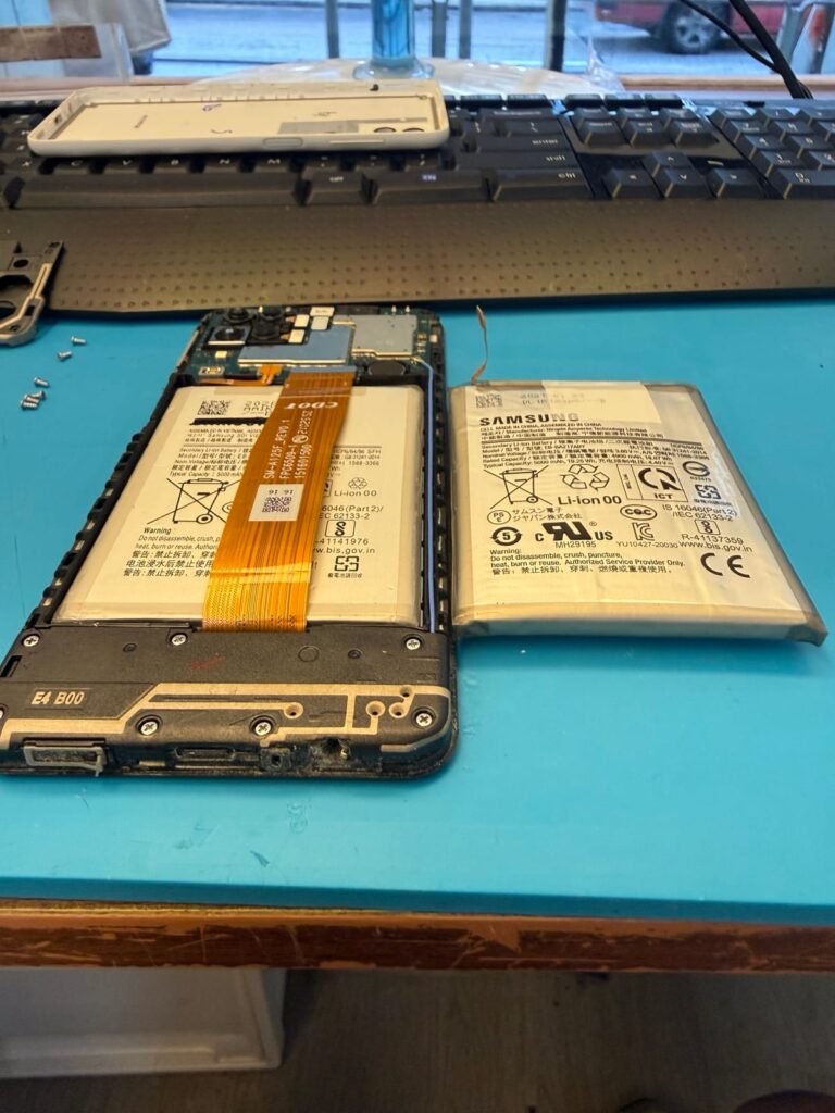 Samsung Galaxy A12 更換電池後的機內狀況，旁邊放著拆出的膨脹舊電池